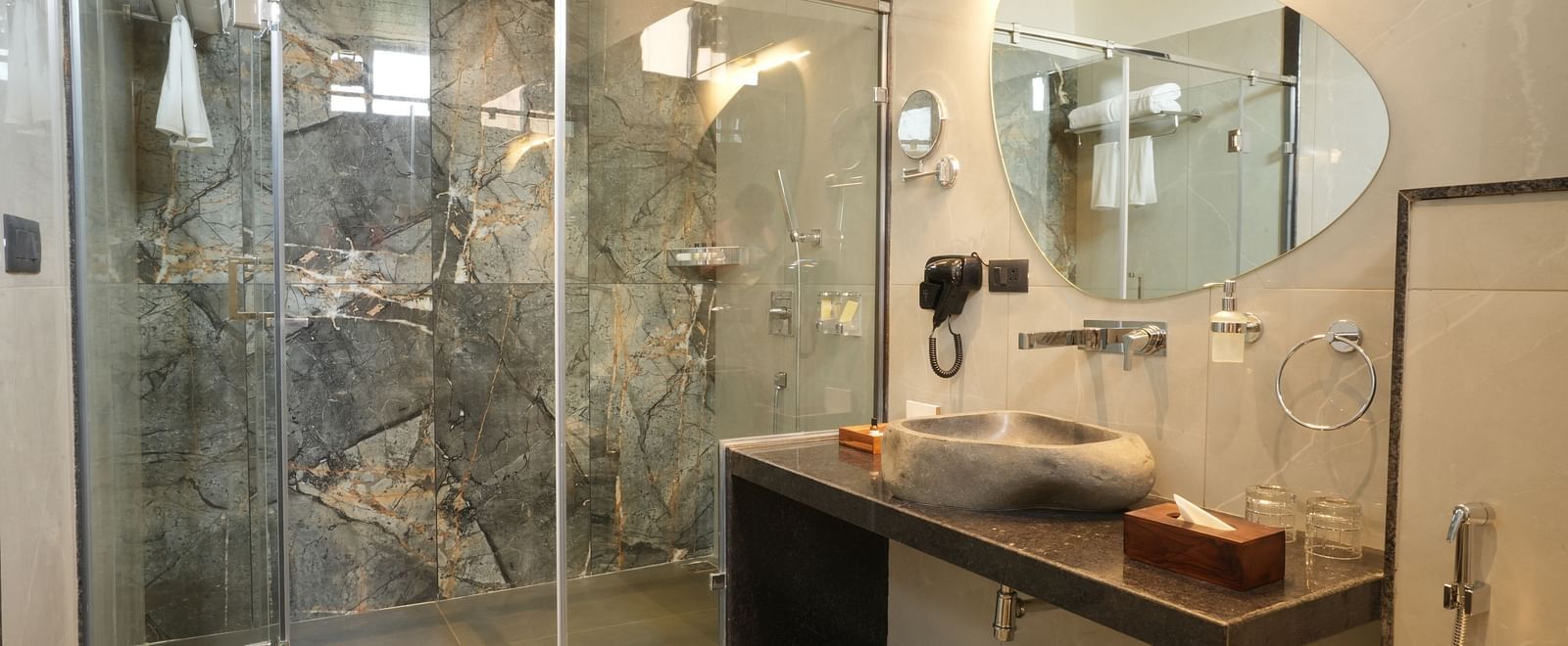 Bathroom of Valley View Room equipped with a glass-enclosed shower, a modern sink, and a round mirror at The Qualia Resort Club & Brewery, Udaipur.