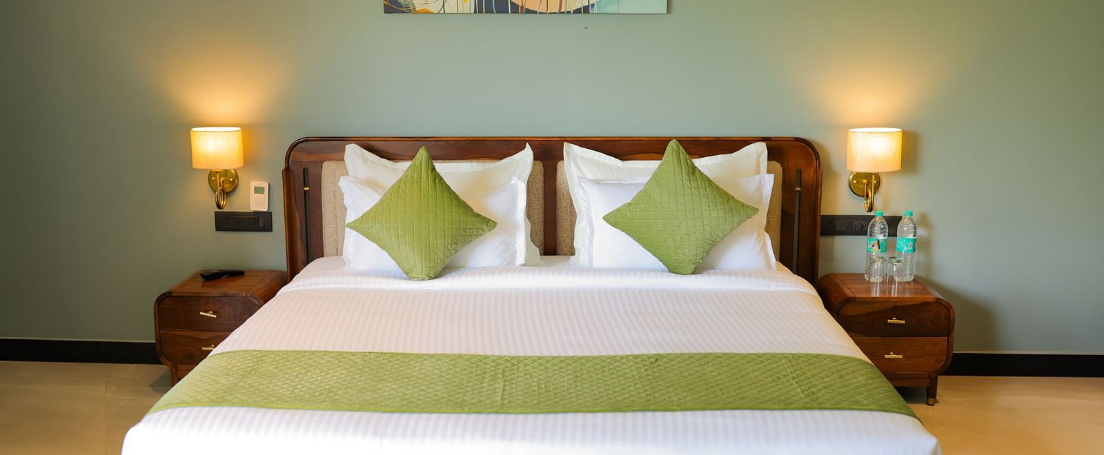 Club Suite with Valley View Sitout featuring a king size bed with white linens and green accents, flanked by bedside tables and lamps at The Qualia Resort Club & Brewery, Udaipur.