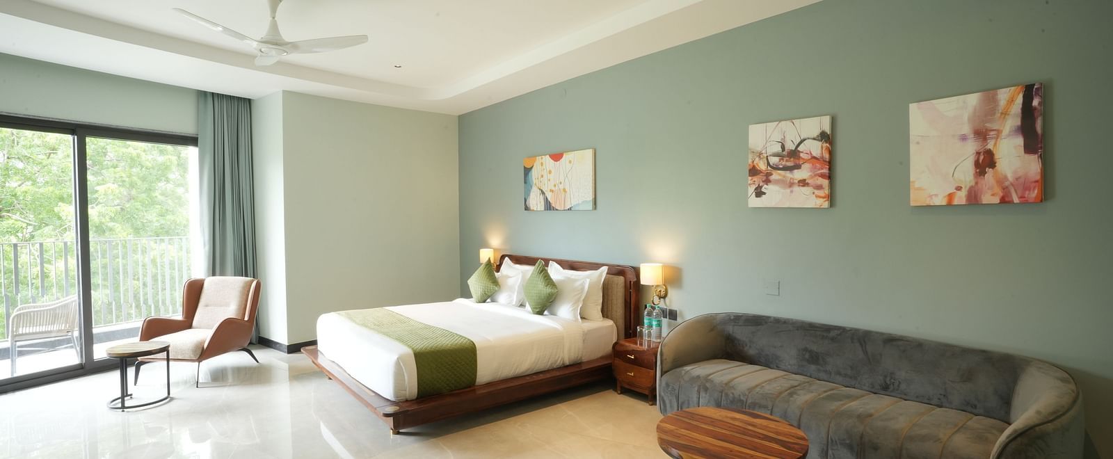 Club Suite with Valley View Sitout featuring a king size bed, couch, and modern decor, with a view of greenery visible through a large window at The Qualia Resort Club & Brewery, Udaipur.