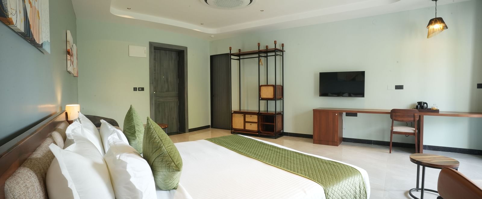 Club Suite with Valley View Sitout featuring a king size bed with white linens and green accents, several pillows, and a wooden headboard at The Qualia Resort Club & Brewery, Udaipur.
