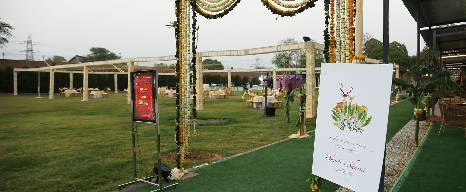 An entrance setup at Tisya Farms, Gurgaon with green flooring, flower decorations, and a welcome board.