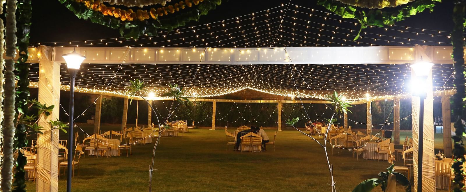 Lawn setup with chairs and lights under a canopy decorated with flowers at Tisya Farms, Gurgaon.