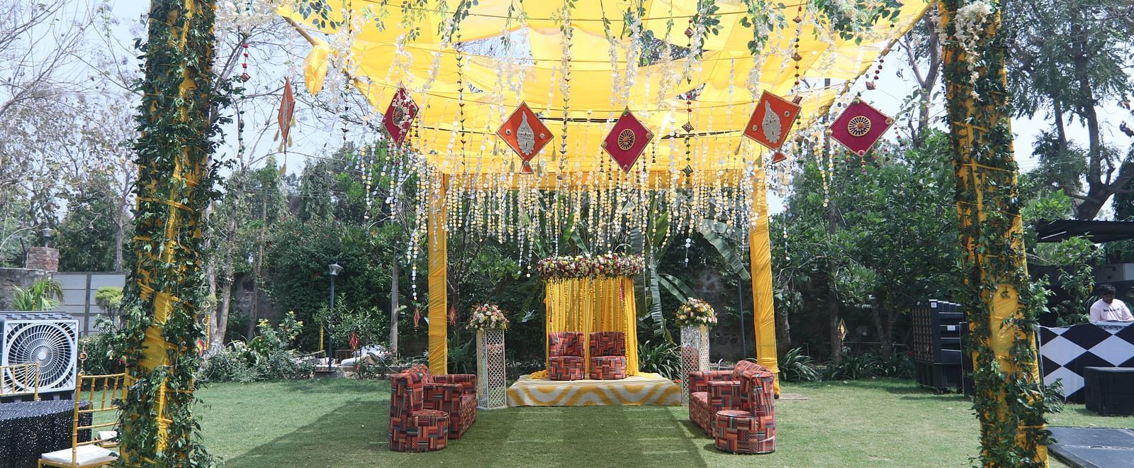 Daytime wedding setup with yellow drapes and floral arrangements at Tisya Farms, Gurgaon.