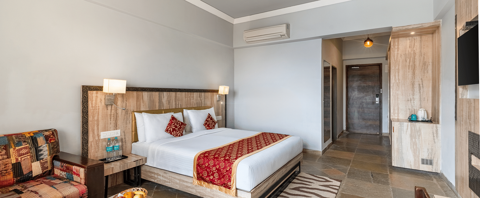A bedroom with with a made bed and pilows on it, beside it is a table and a chair neatly arranged - Via Lakhela Resort & Spa