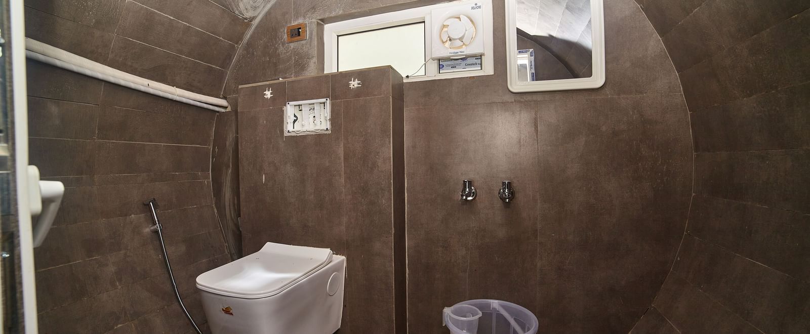 The interior of a compact, dark grey bathroom, likely within a capsule unit, featuring a toilet, a small sink, and a mirror on the wall. - Vintage Trails by Ilara