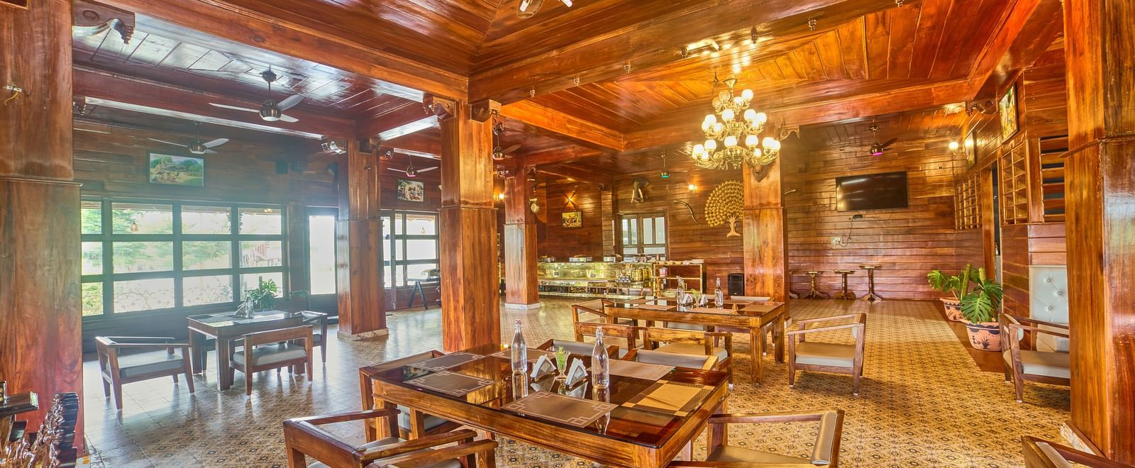 A spacious, warmly lit dining or common area with polished wooden floors, intricate wooden ceilings, and numerous tables and chairs, offering a panoramic view of the space. - Vintage Trails by Ilara