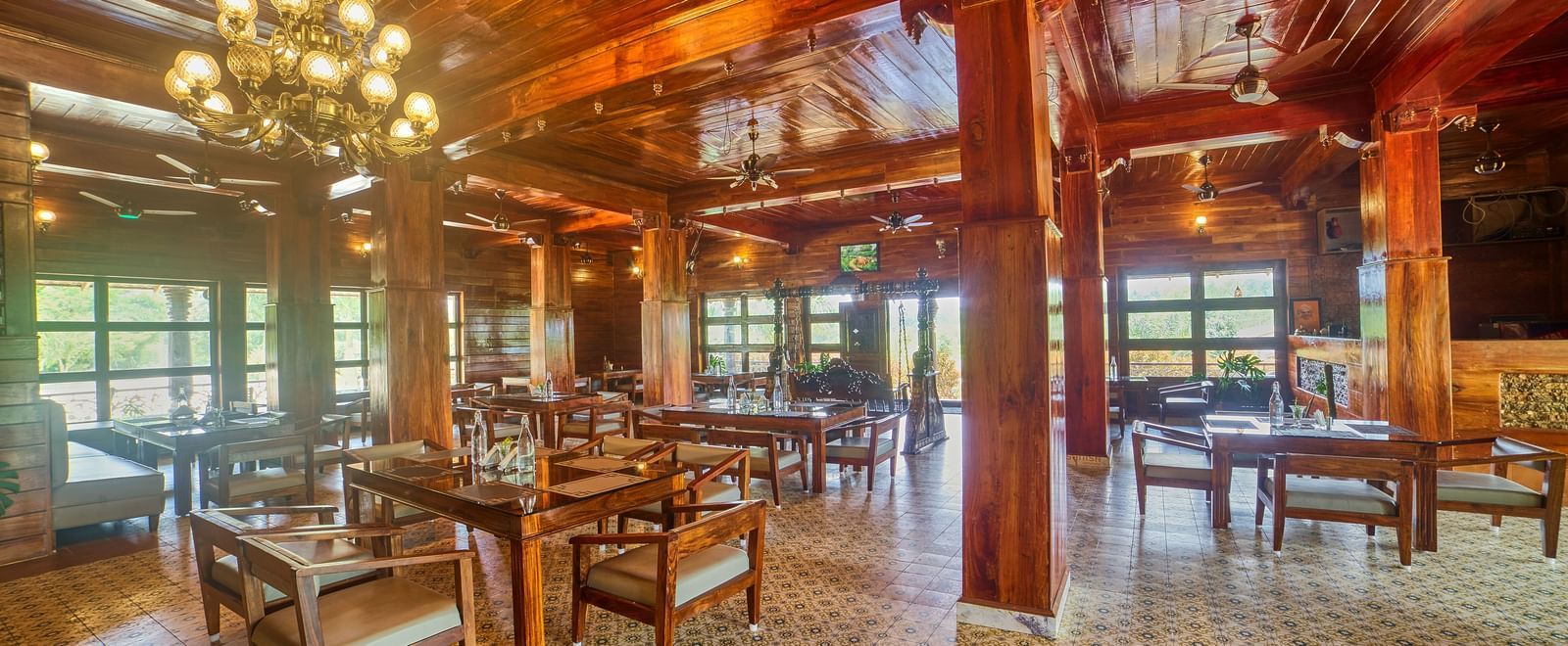 A spacious, rustic-style dining or common area with polished wooden floors, exposed wooden beams and columns, and multiple tables and chairs set up for guests. - Vintage Trails by Ilara