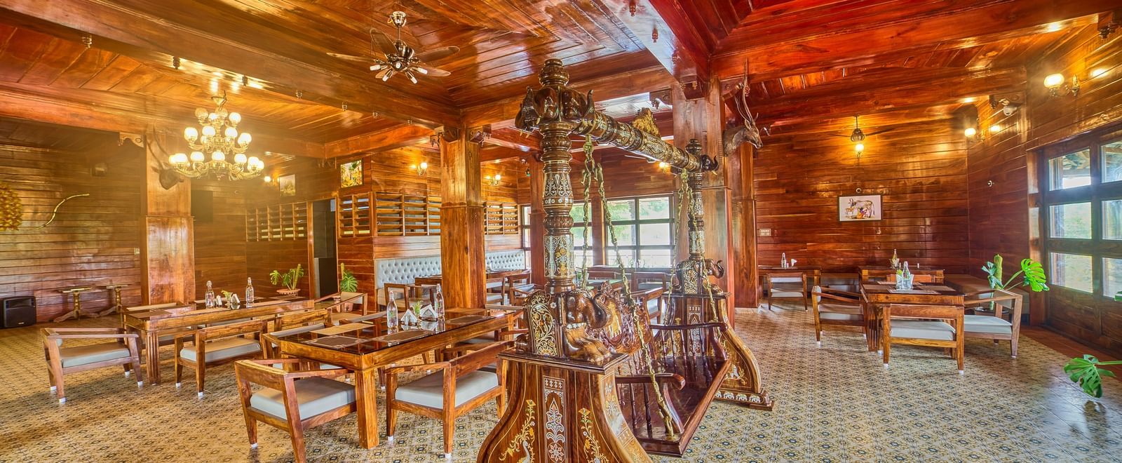 A spacious, rustic-style dining or common area with polished wooden floors, exposed wooden beams and columns, and multiple tables and chairs set up for guests, viewed from a different angle. - Vintage Trails by Ilara