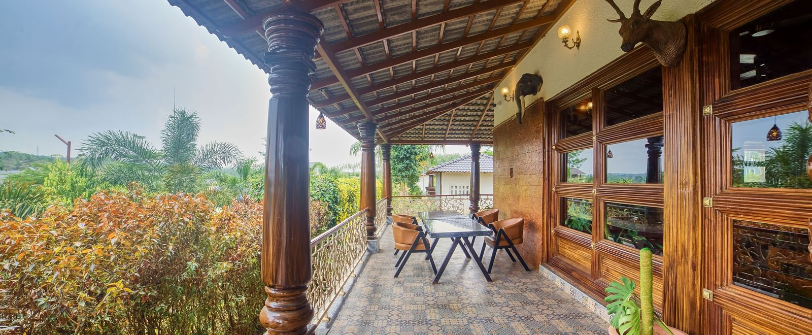 A covered outdoor veranda with wooden pillars, featuring a small table and chairs amidst lush greenery. - Vintage Trails by Ilara