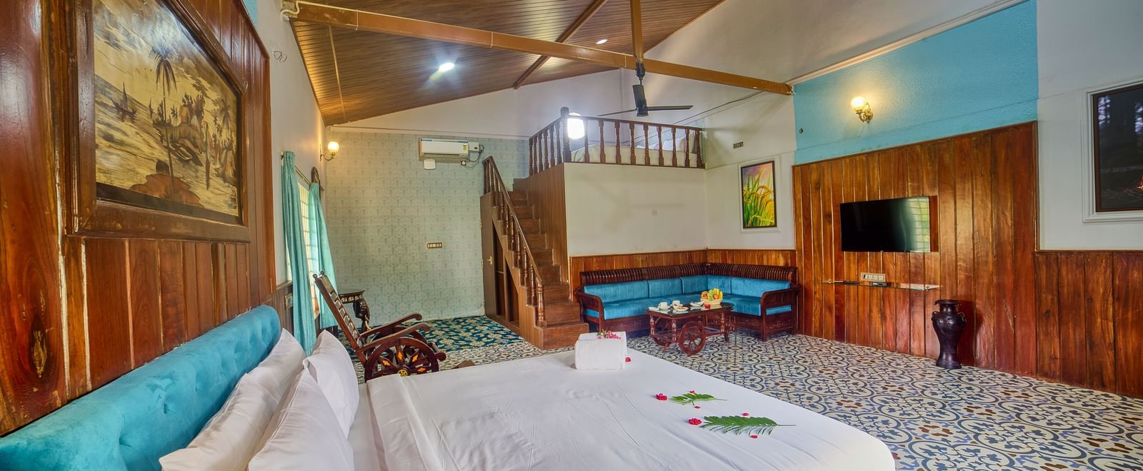 A spacious hotel room with a white bed, patterned tiled floor, and wooden ceiling, showing a sitting area with a blue sofa and a television. - Vintage Trails by Ilara