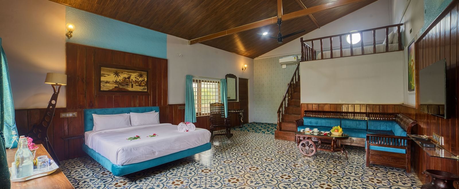 The interior of a bedroom or common area with a patterned tiled floor, a large bed with a light blue bedspread, and ceiling, and a seating area with a sofa. - Vintage Trails by Ilara