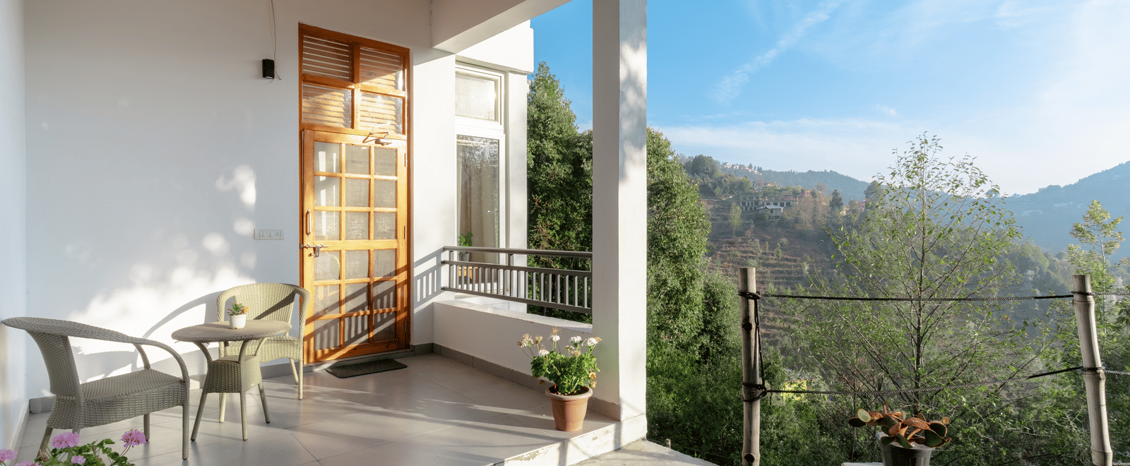 The front porch of Ziran Retreat, showing a sitting area with chairs and a table, overlooking a mountain landscape on a sunny day.