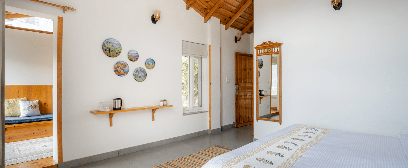 A bedroom at Ziran Retreat, showing a bed with a white comforter, a headboard with wall lamps, and a unique mirror and wall decor on the right side.