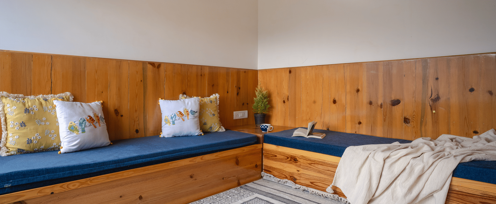 A close-up shot of the daybed area in Ziran Retreat's bedroom, showing the blue cushioned seat with colorful pillows, and the wooden paneling on the wall.