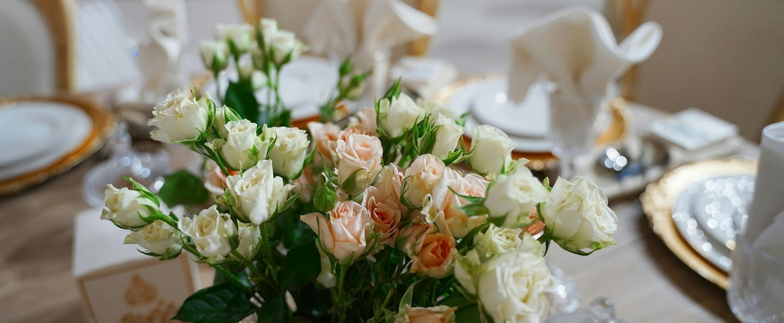 A close up shot of a beautiful flower vase with a lot of white and pink roses on a dining table.