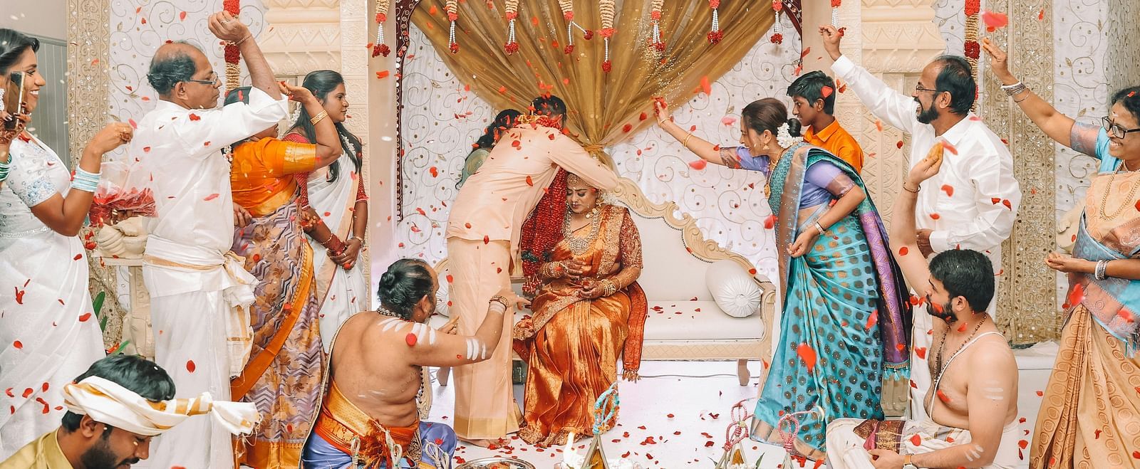 A stage with a vibrant South Indian wedding taking place where the broom is tying a mangalsutra (sacred matrimonial thread) around the bride's neck.