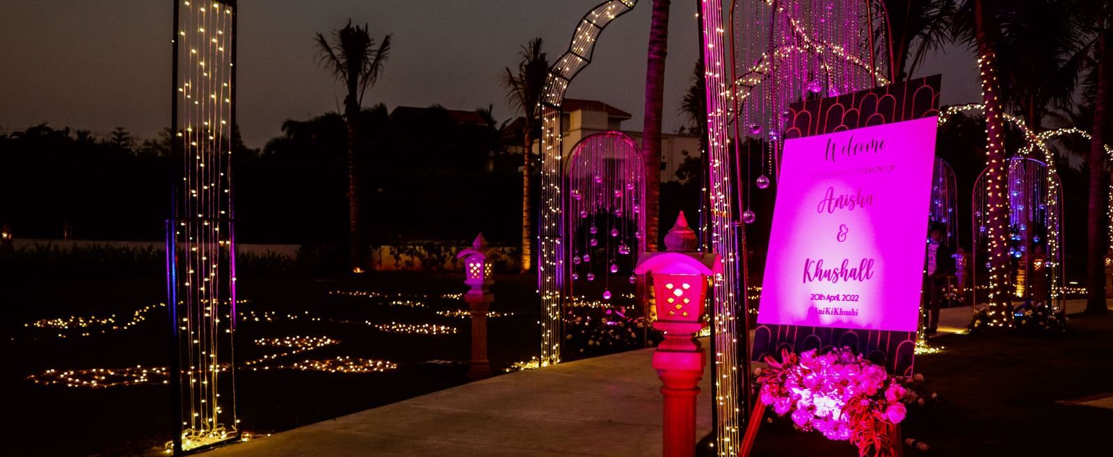 The entrance to the Sangeet of ANisha & Kushaal featuring arches filled with lights and a singboard with the name of the event and the groom and bride at the Lawn of Kaldan Samudhra Palace