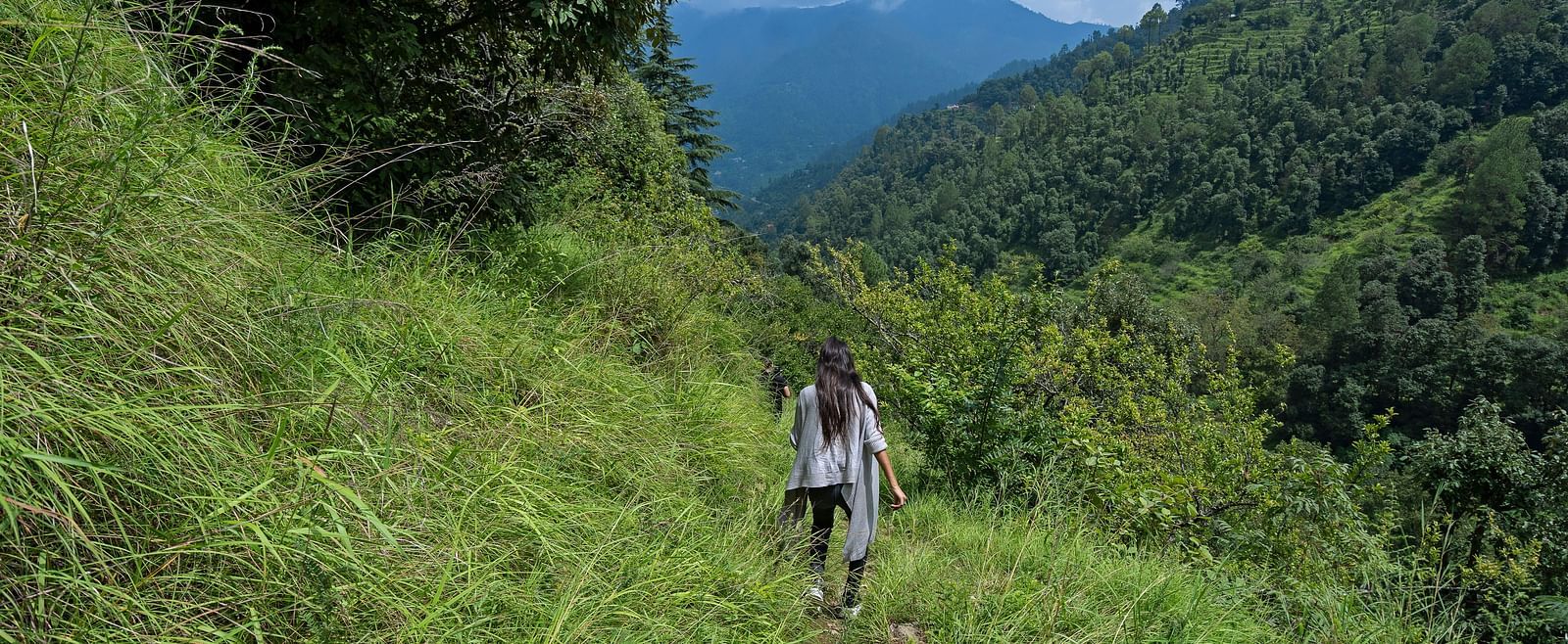 Couple trekking through a grassy trail surrounded by mountains and forest, at BluSalzz Collection - Suvaasa Resort, Ramgarh.