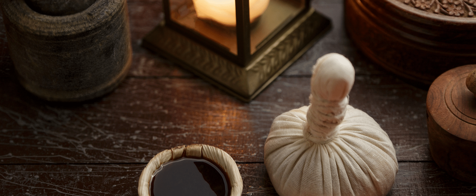 A still featuring spa or wellness items on a dark wooden surface, including a poultice and pestle, candles, and a small bowl.