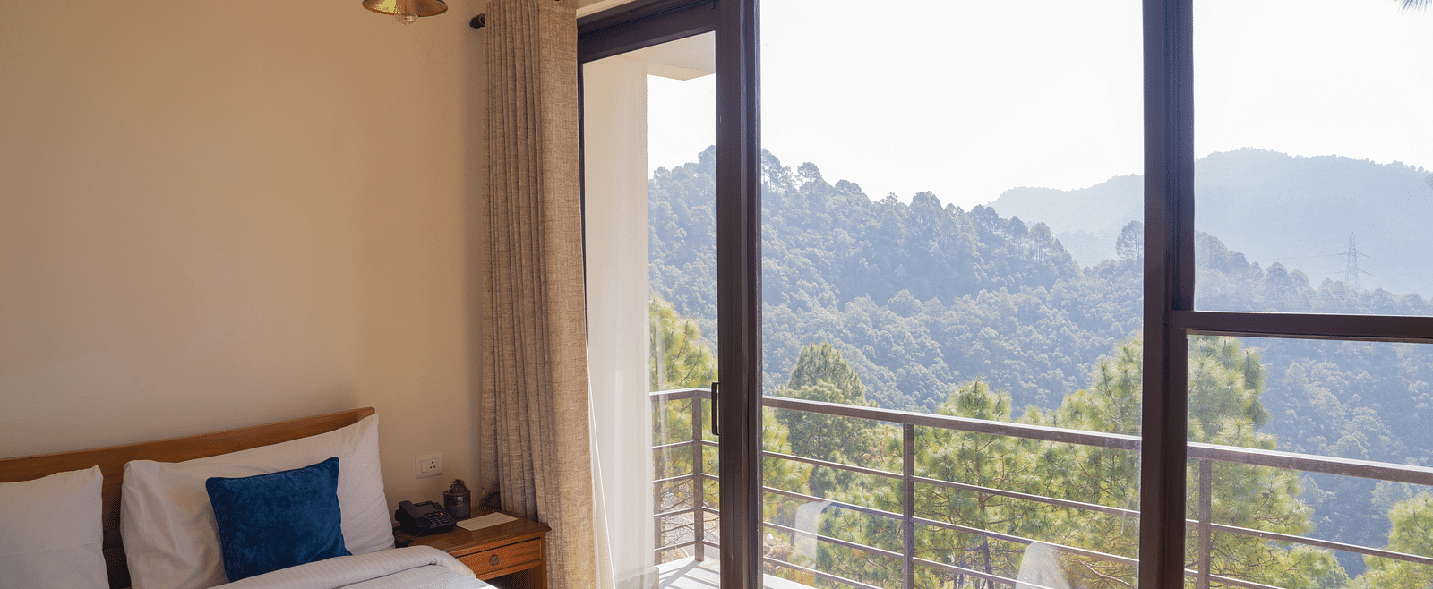 A bedroom with a balcony offering mountain views at BluSalzz Escapade Resort, Lansdowne.