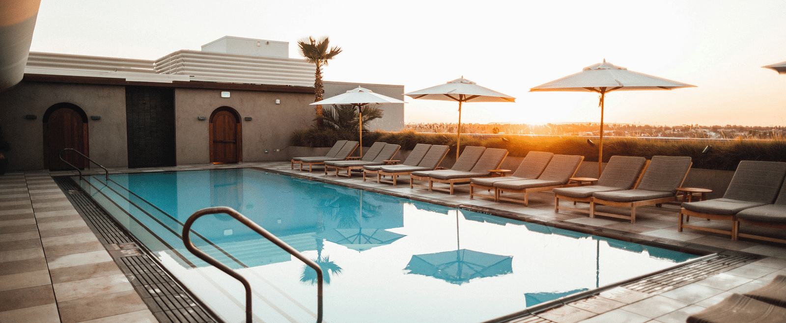 An image of a swimming pool featuring sun loungers seen during a sunset