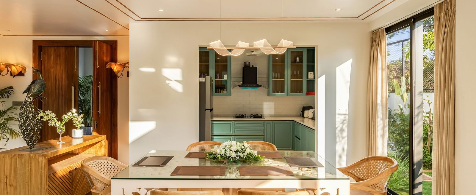 A dining area with a wooden table and chairs, complemented by natural light and an open-plan design connected to the kitchen - BluSalzz Villas - Alocassia, Anjuna