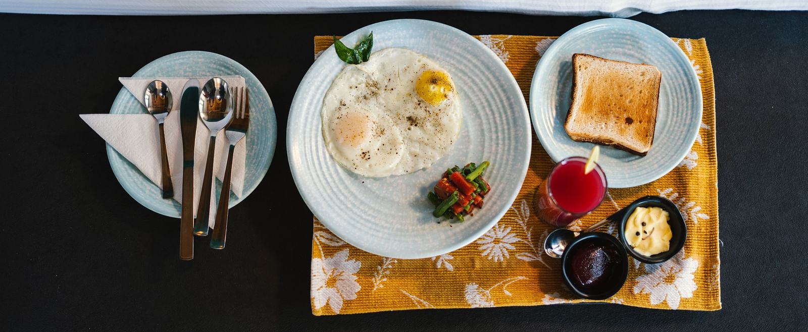 A top view of three plates at BluSalzz Villas - The Green Roof, Bhimtal, featuring toast, an omelette with vegetables, and cutlery alongside jam, butter, and a lit candle.