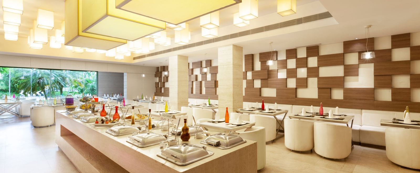 A diagonal view of a restaurant with an island in the middle featuring buffet items, surrounded by tables and chairs on the sides | Cenneys Gateway