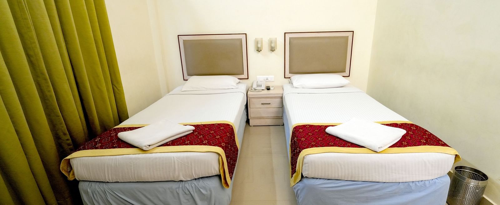 A hotel twin bedroom with white and mustard bedding, green curtains, and a picture on the wall at Greens Inn - Comfortable Twin Rooms in Ramoji Film City.