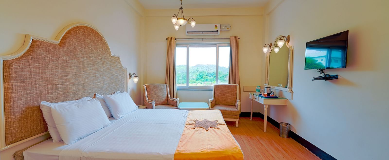A well-appointed hotel room with a large bed, orange throw, wooden flooring, and a TV. - Greens Inn - Cozy Accommodations