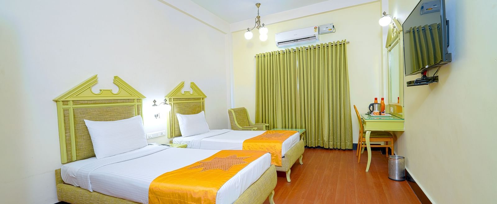 A twin hotel room with light wooden flooring, green headboard, and mustard accents, offering a cozy atmosphere at Greens Inn - Cozy Twin Rooms in Ramoji Film City.