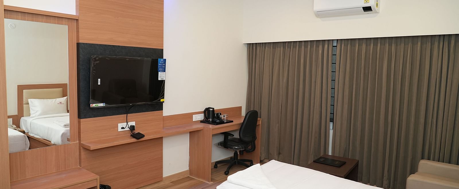 a bedroom with modern furnishings featuring a twin bed along with a medium mirror and a wall mounted television opposite to it - Hotel Grand Sigma