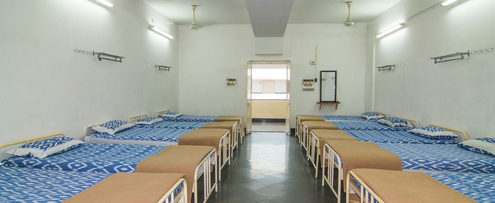 A full view of beds with bedding arranged in two rows in a room | Hotel Sahara