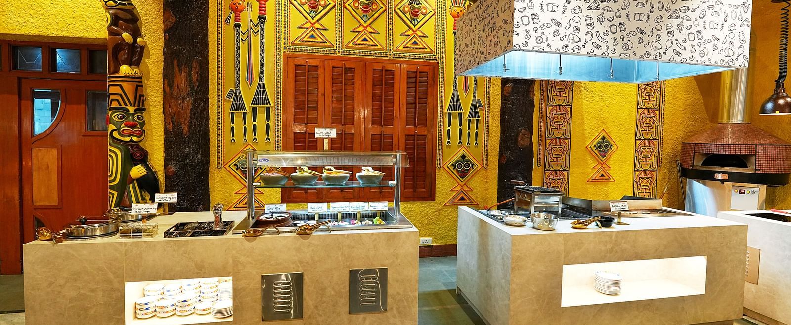 A buffet area with traditional design elements, wood carvings, and ambient lighting at Tara, Comfort Hotel in Hyderabad - Ramoji Film City.
