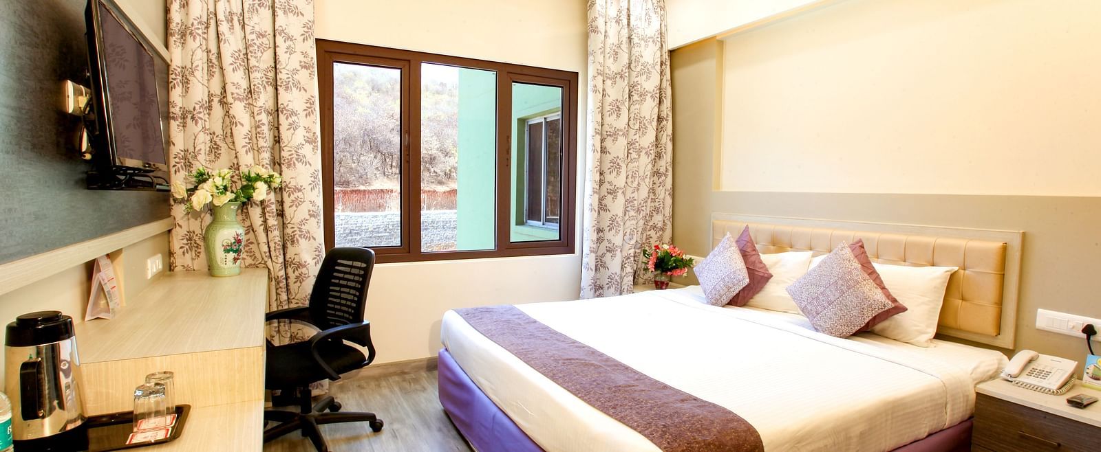 A modern hotel room with a plush king-sized bed and a view of the outdoors. - Tara, Comfort Hotel in Hyderabad - Ramoji Film City.