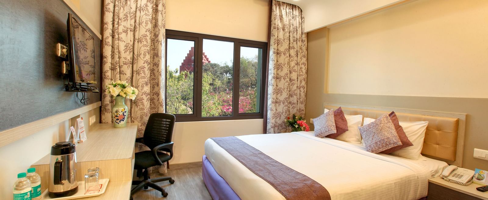 A spacious and elegantly decorated hotel room with a large window and a work area. - Tara, Comfort Hotel in Hyderabad - Ramoji Film City.