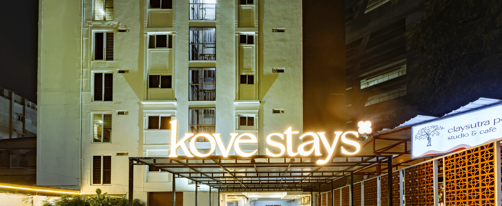 A closer view of the multi-storey Kove Smart Stays seen during the night, with its large logo illuminating the words 'Kove Stays'.