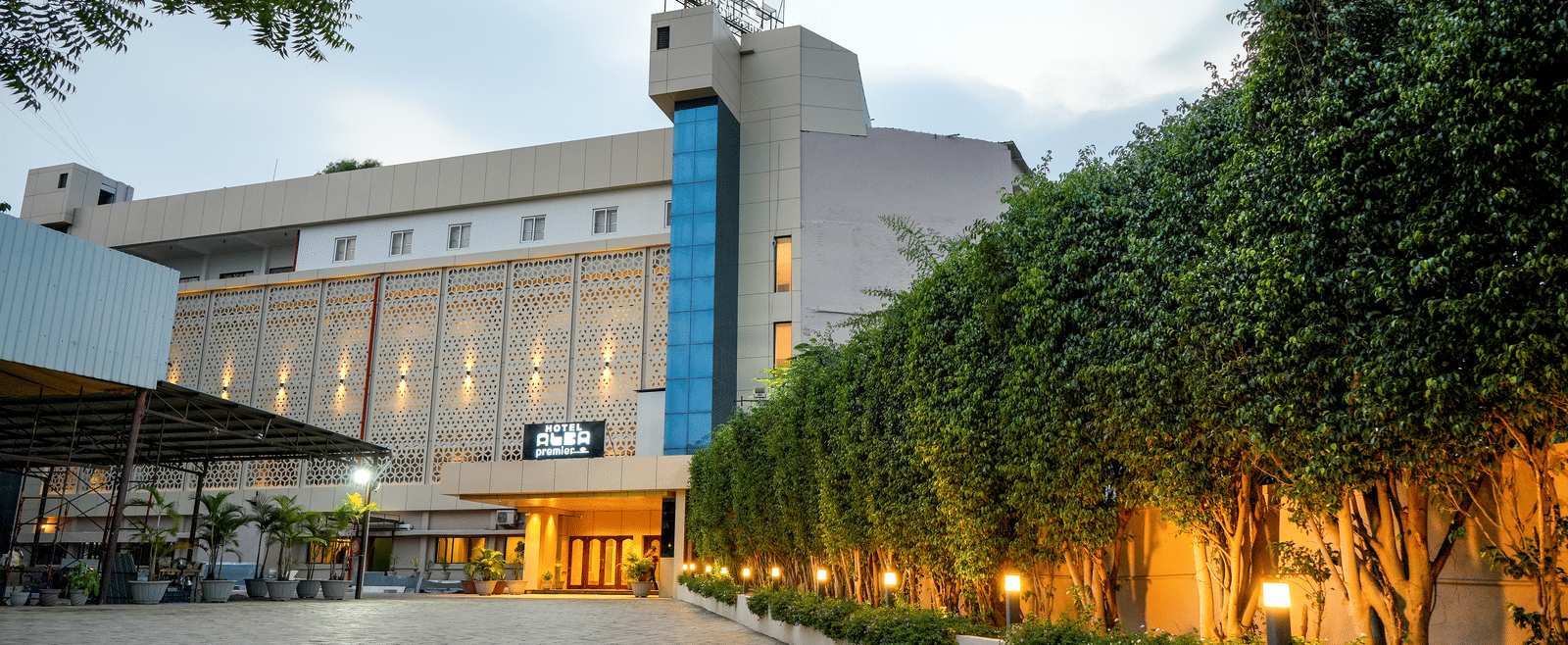 Exterior view of hotel building with driveway and trees at Pravasa Hotel, Kolhapur.