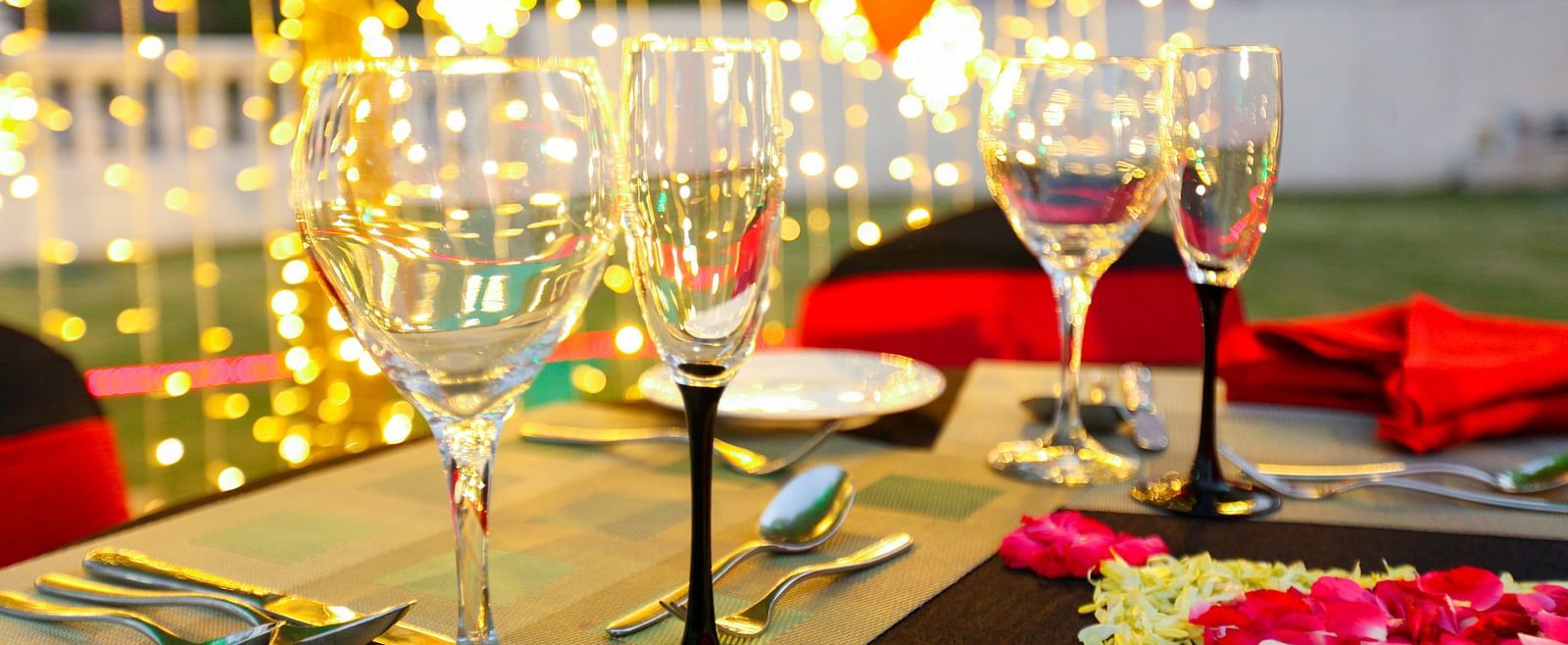 glasses set on a table with plates, cutlery and decoratations in the backdrop - Ramoji Film City Hotels in Hyderabad 