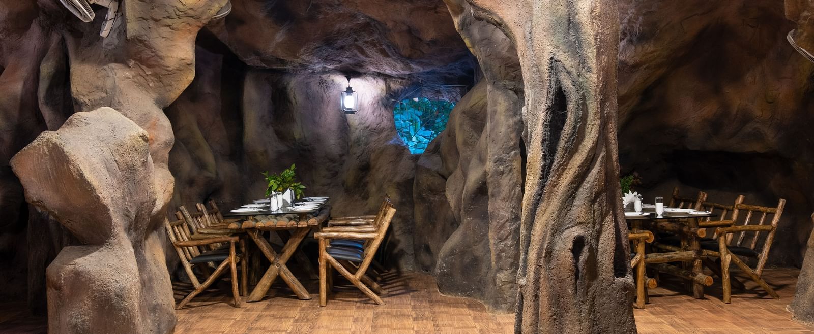 A cave-themed restaurant shows more seating arrangements with wooden tables and chairs amidst sculpted rock walls | Cave Restaurant