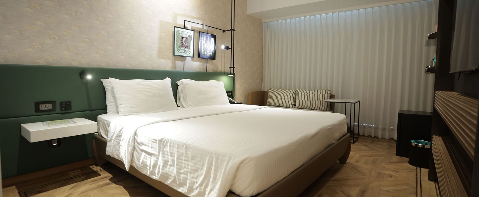 Modern guest room at Regency Hotel, Mumbai with plush bedding, contemporary furniture, large windows and elegant green accent wall for a comfortable stay.
