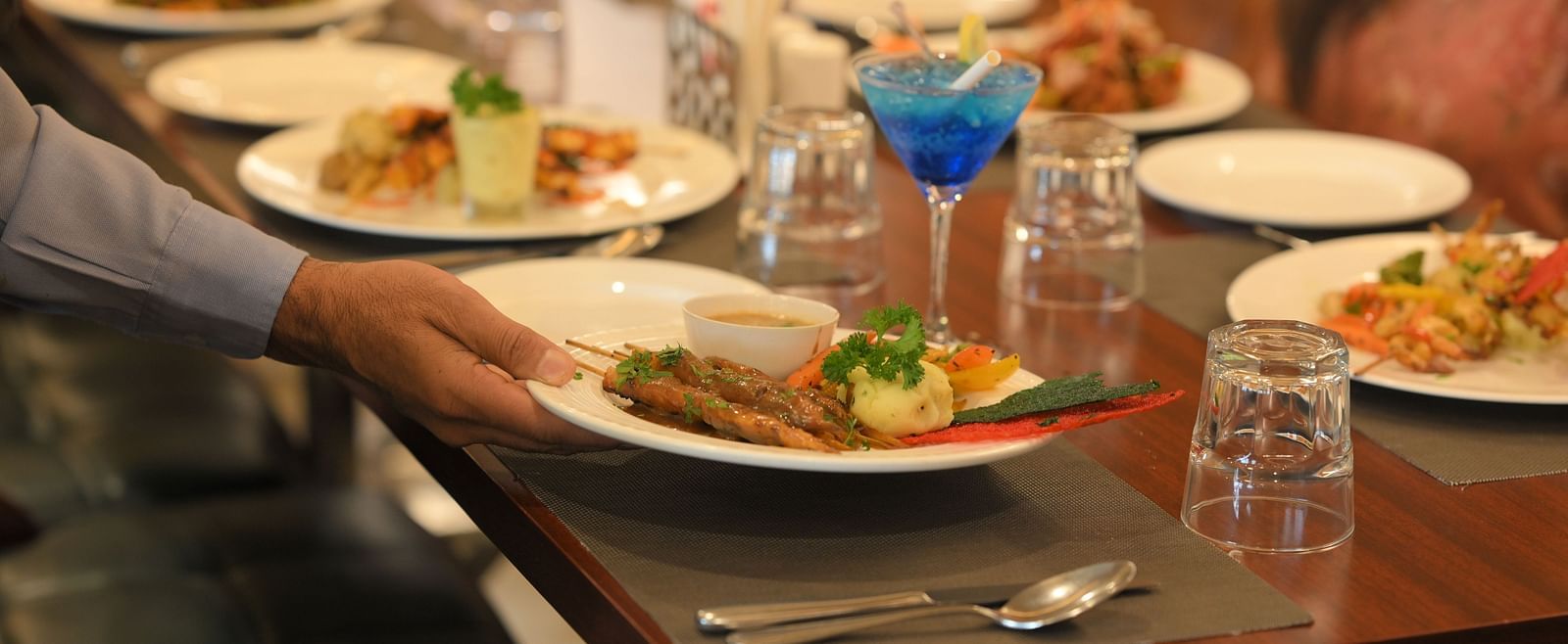 Attentive staff serving a table with beautifully arranged dishes for guests at Royal Comfort Regency.