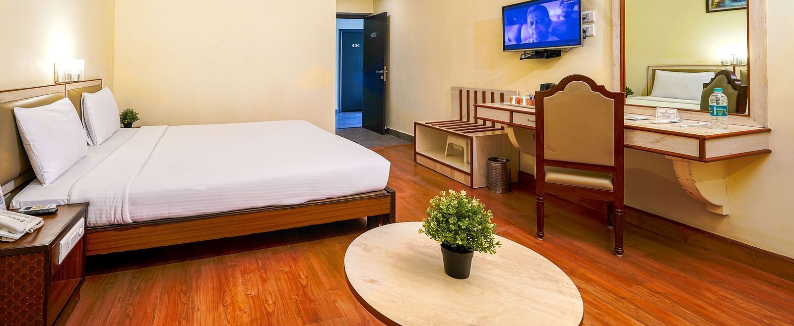 Spacious hotel room with a double bed, wooden flooring, flat-screen TV, and work desk in Hyderabad near Ramoji Film City.