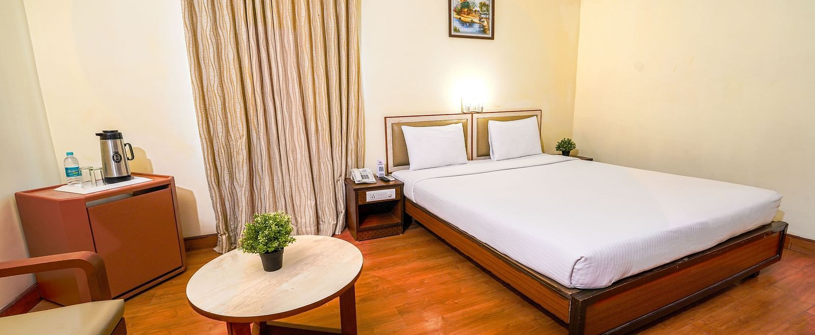 Bright hotel room with a double bed, wooden flooring, and a seating area by the window in Hyderabad near Ramoji Film City.