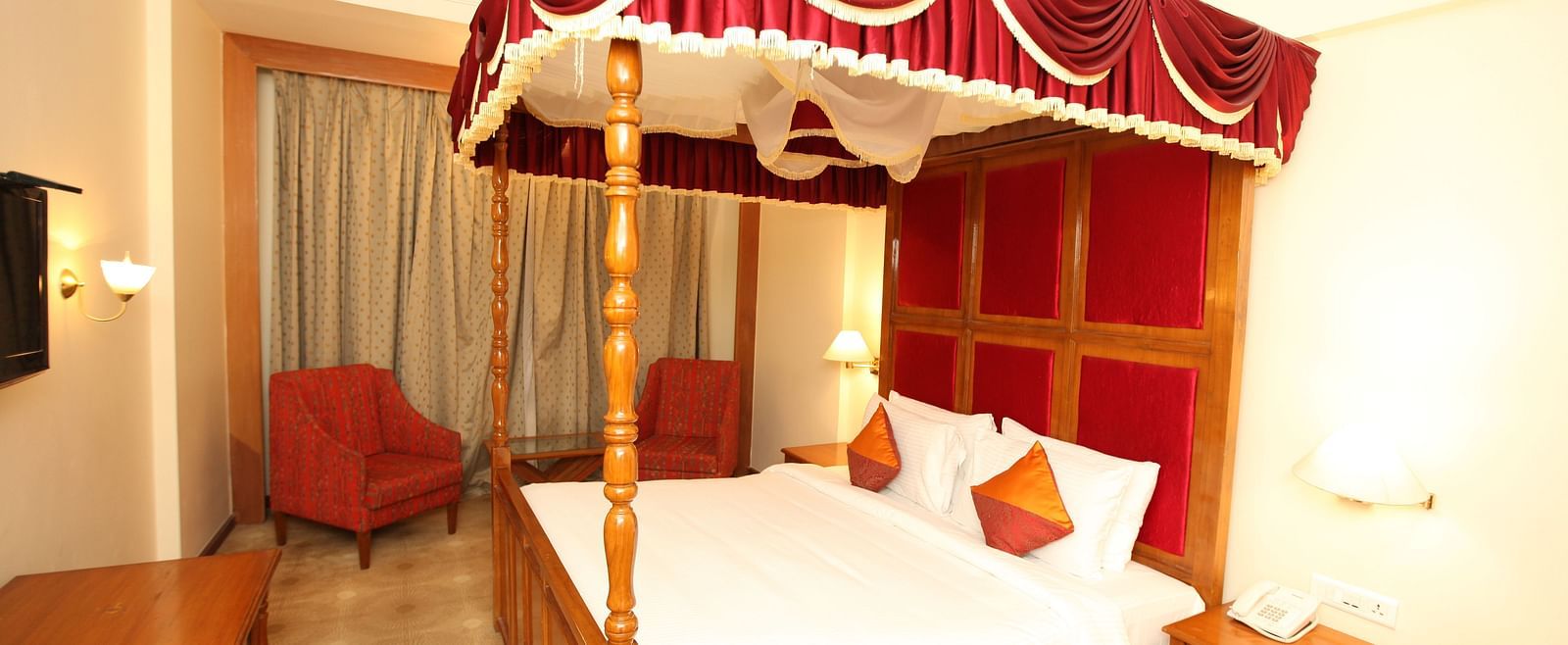 A luxurious hotel room with a red canopy bed, highlighting comfort and opulence at  Sitara Luxury Hotel in Hyderabad near Ramoji Film City.