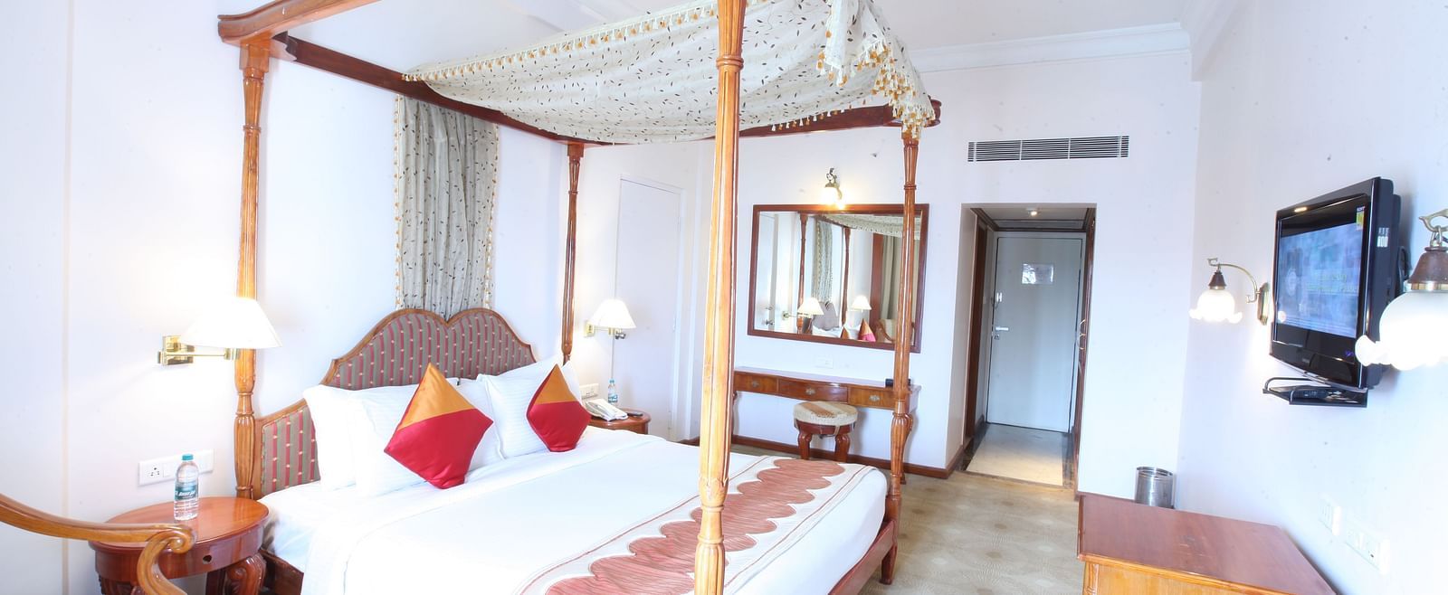 A well-lit hotel room with a four-poster bed, elegant decor, and ample space for relaxation at  Sitara Luxury Hotel in Hyderabad near Ramoji Film City.