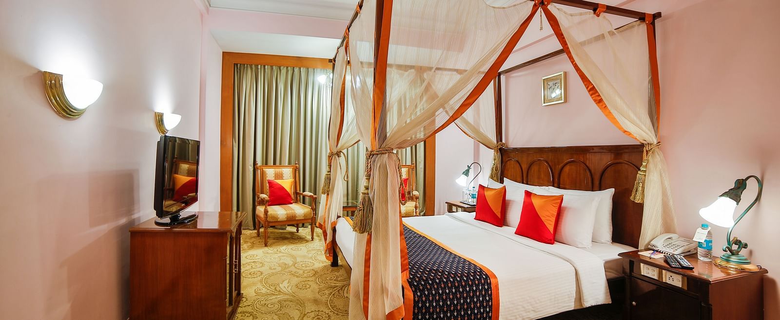 A spacious hotel room with a four-poster bed draped in sheer curtains, providing a serene atmosphere at  Sitara Luxury Hotel in Hyderabad near Ramoji Film City.