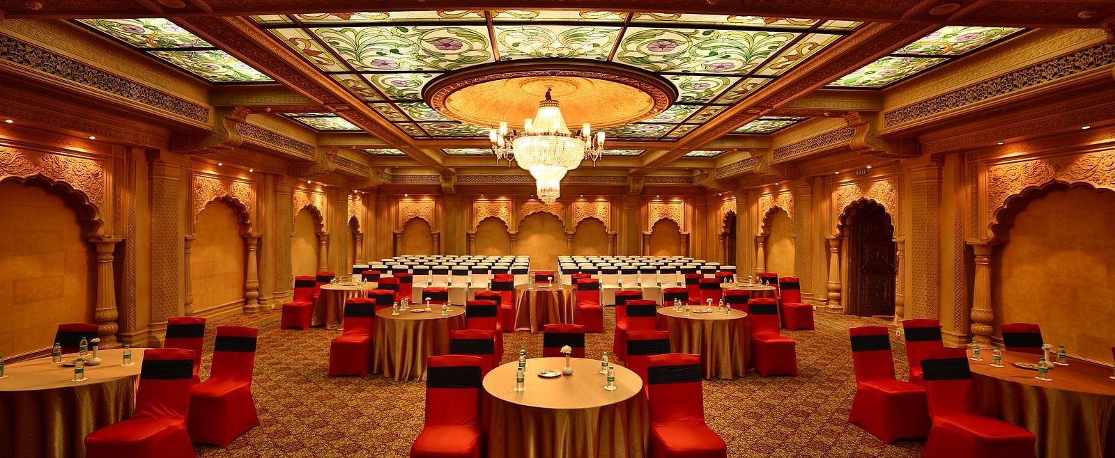 Seating arrangement in Taj Mahal Hall A grand hotel suite with an opulent red and white decor, large bed, and seating area, reflecting a traditional style at Sitara Luxury Hotel in Hyderabad near Ramoji Film City.