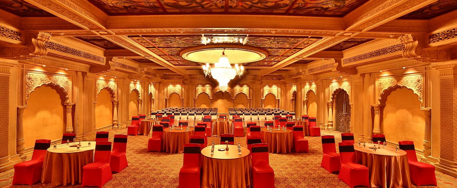 Seating arrangement in Taj Mahal Hall A grand hotel suite with an opulent red and white decor, large bed, and seating area, reflecting a traditional style at Sitara Luxury Hotel in Hyderabad near Ramoji Film City.