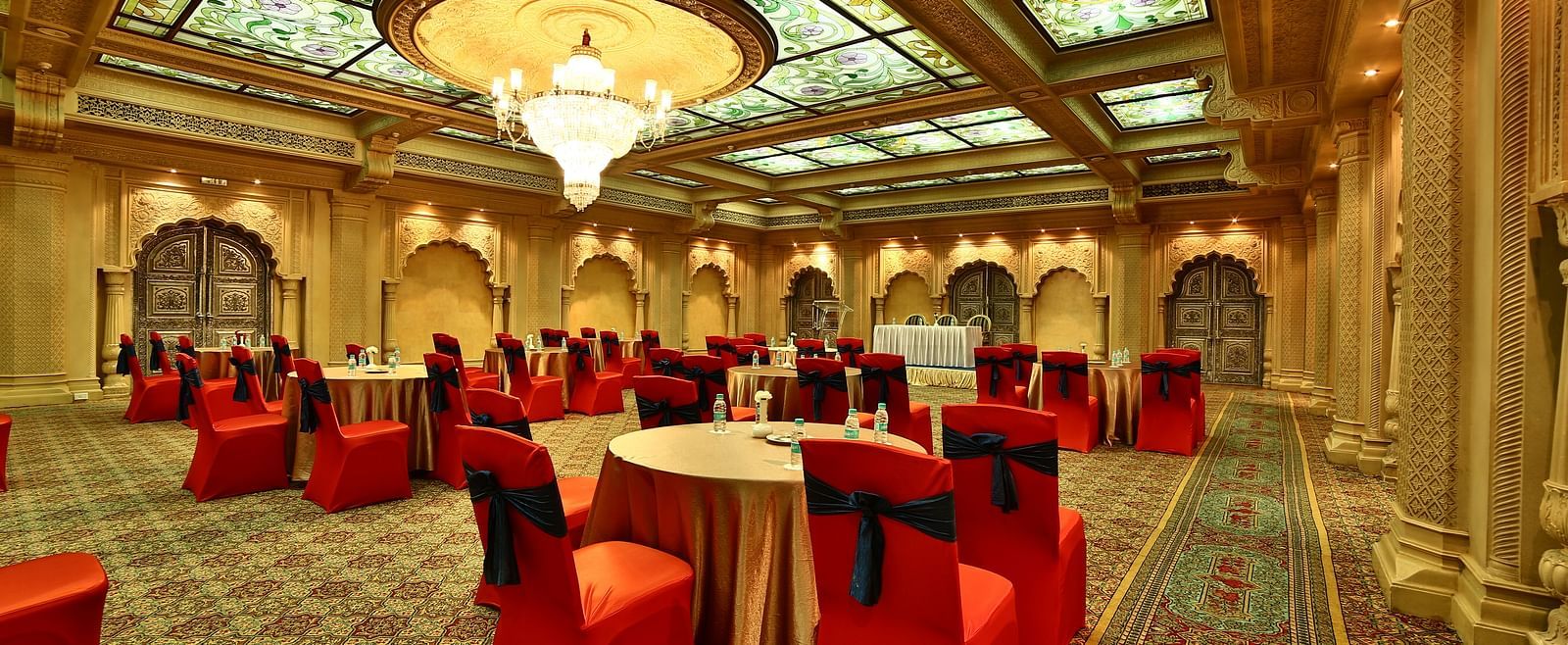 Seating arrangement in Taj Mahal Hall A grand hotel suite with an opulent red and white decor, large bed, and seating area, reflecting a traditional style at Sitara Luxury Hotel in Hyderabad near Ramoji Film City.